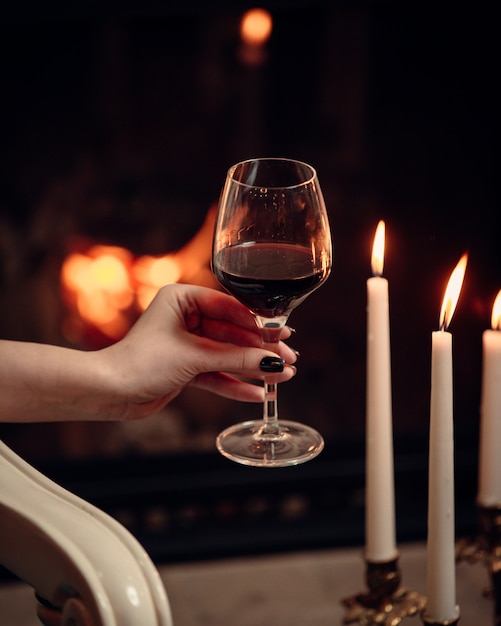 A glass of red wine held beside candlelight