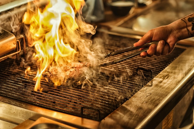 Chef turning a steak over the flames of the open grill